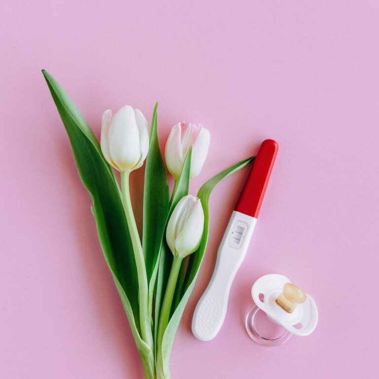 Test de grossesse positif sur fond rose avec tétine bébé et tulipes - début de grossesse